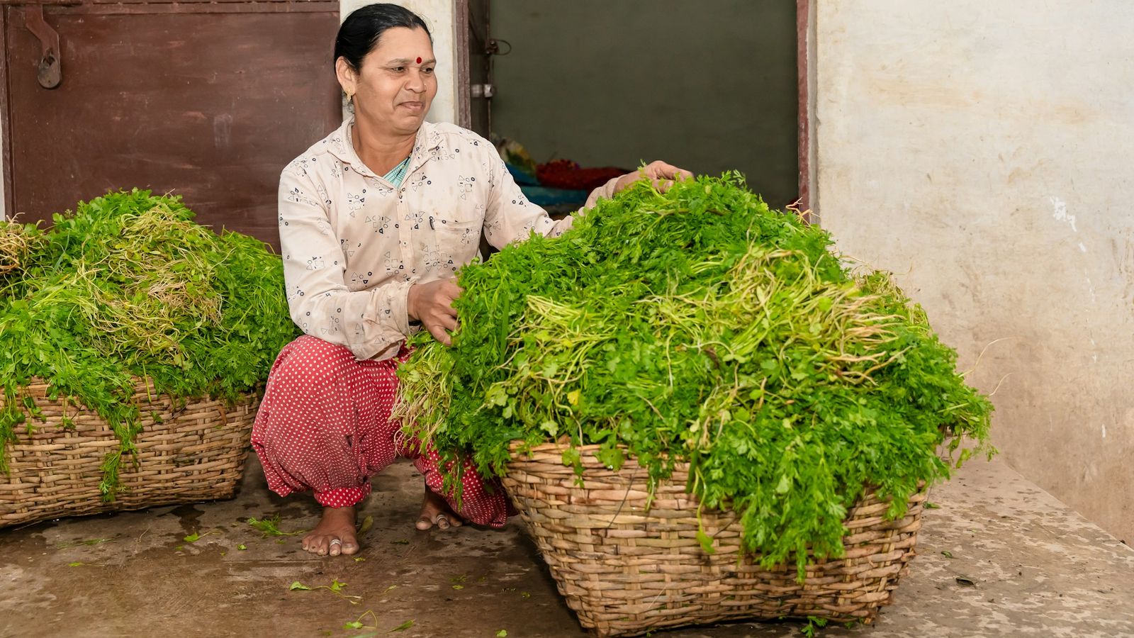 A woman in India sitting beside large baskets of fresh green leafy vegetables