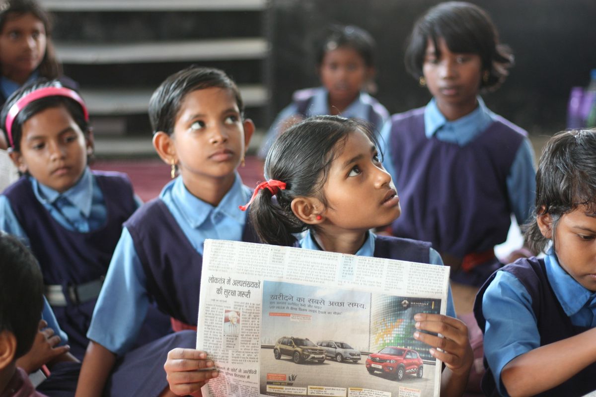 A schoolgirl in an Indian classroom reading a newspaper with her classmates