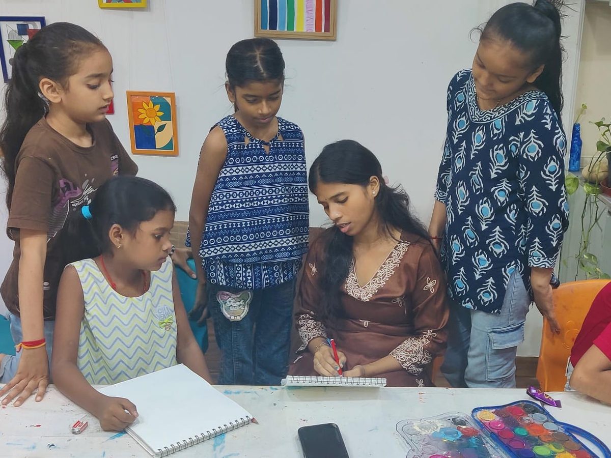 Girls drawing in sketchbooks with their art teacher at a table