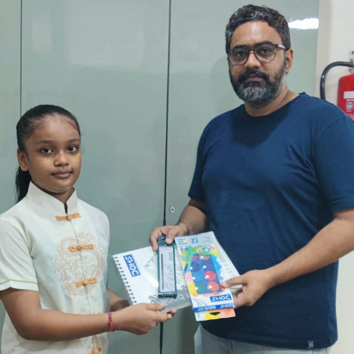 A man handing art supplies and a sketchbook to a young student